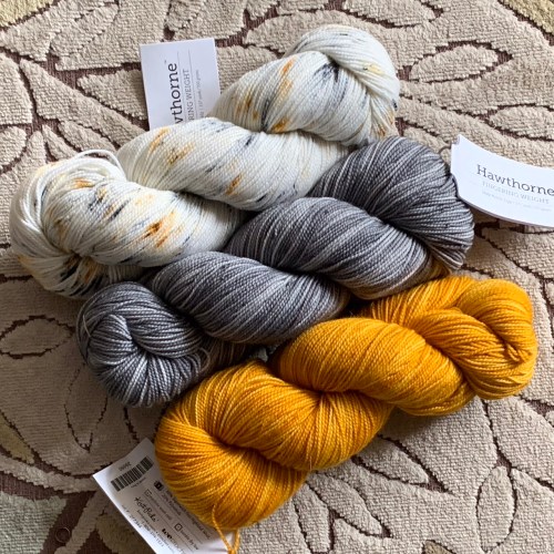 3 skeins of yarn: white speckle, gray, and yellow