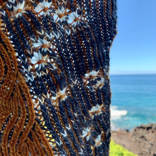 A piece of knitting being held in the air with the ocean in the background