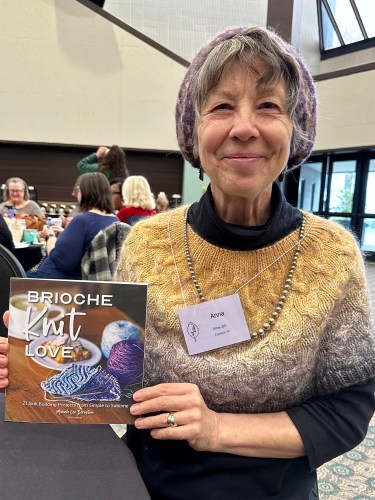 woman wearing a knit sweater and hat, holding a book about knitting, Brioche Knit Love by Michele Lee Bernstein