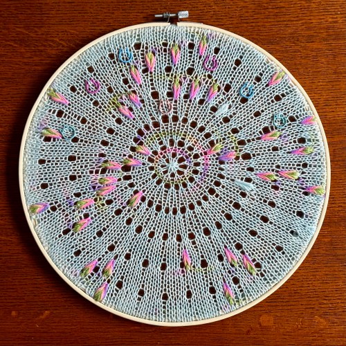 A knit circle featuring assigned pooling motifs on an embroidery hoop
